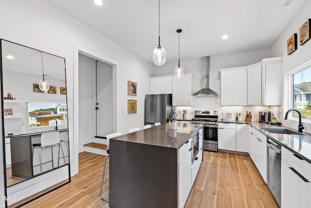 kitchen with a sink, wall chimney exhaust hood, white cabinetry, decorative backsplash, and appliances with stainless steel finishes
