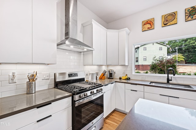 kitchen with sink, stainless steel range with gas cooktop, wall chimney range hood, white cabinetry, and light hardwood / wood-style flooring