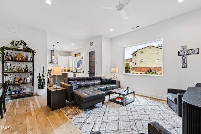 living room with bar area, light wood-type flooring, and ceiling fan