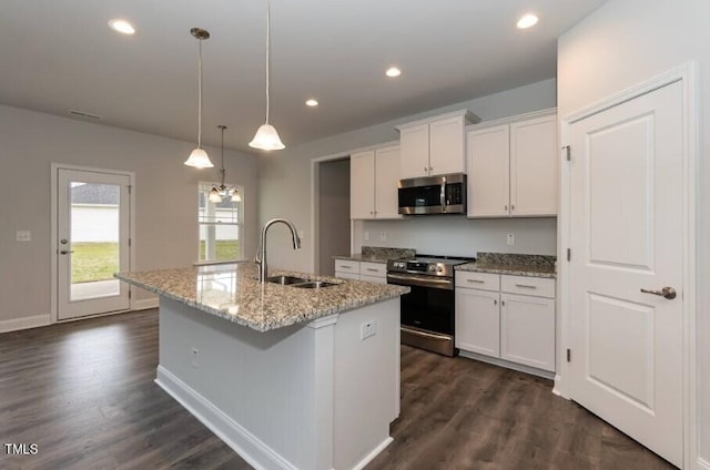 kitchen with an island with sink, appliances with stainless steel finishes, hanging light fixtures, white cabinets, and sink