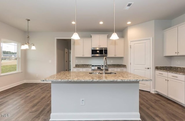 kitchen with white cabinetry, an island with sink, hanging light fixtures, light stone countertops, and sink