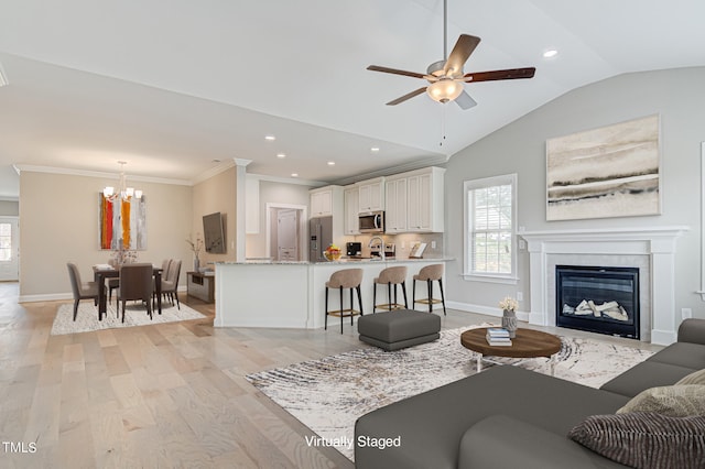 living room featuring ornamental molding, light wood-type flooring, lofted ceiling, and ceiling fan with notable chandelier