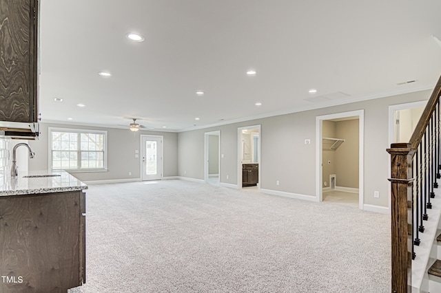 unfurnished living room featuring ceiling fan, ornamental molding, light colored carpet, and sink