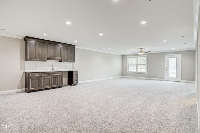 unfurnished living room featuring indoor wet bar, ornamental molding, ceiling fan, and light carpet