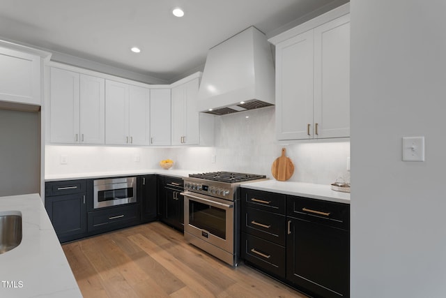 kitchen featuring tasteful backsplash, stainless steel appliances, light wood-type flooring, custom range hood, and white cabinets