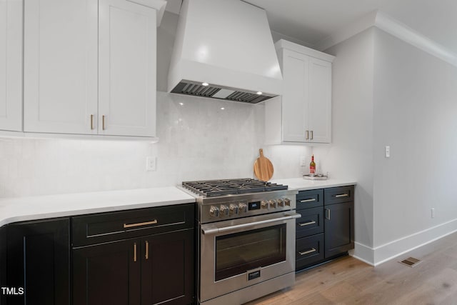 kitchen featuring high end range, custom exhaust hood, crown molding, white cabinetry, and light hardwood / wood-style flooring