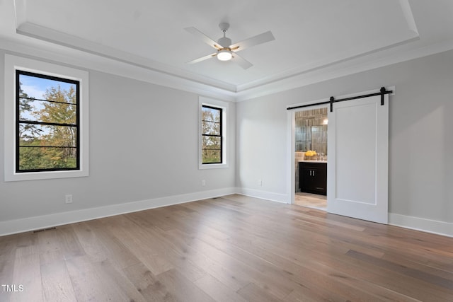 empty room with light wood-type flooring, a tray ceiling, and a barn door