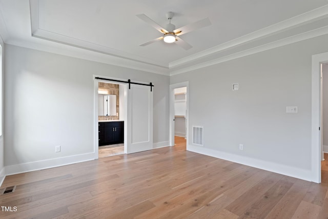 unfurnished bedroom with light hardwood / wood-style flooring, a barn door, and a walk in closet