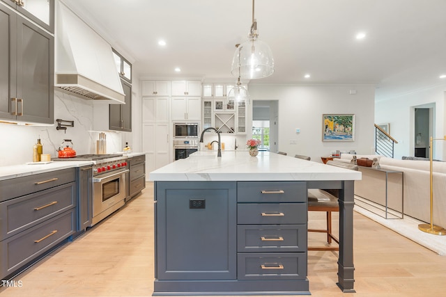 kitchen with appliances with stainless steel finishes, a spacious island, white cabinetry, custom range hood, and pendant lighting