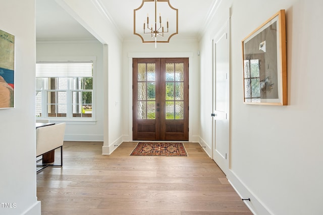 entrance foyer with french doors, light hardwood / wood-style flooring, crown molding, and a chandelier