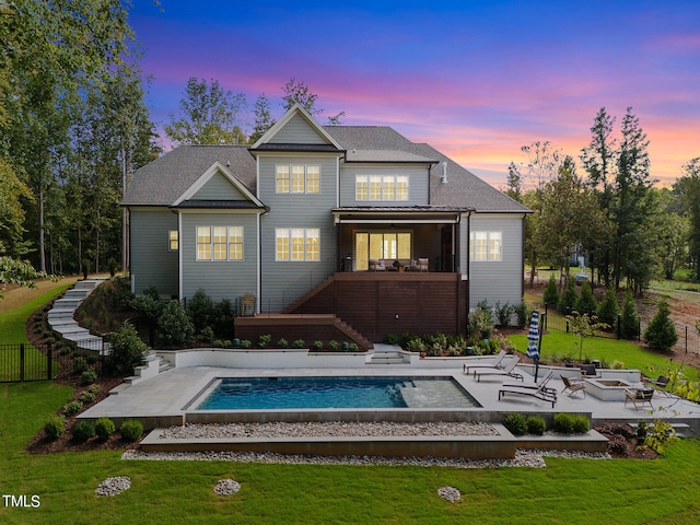 back house at dusk featuring a patio area, a lawn, and a swimming pool with hot tub