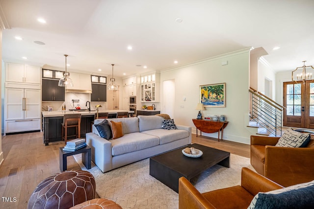 living room with sink, crown molding, light hardwood / wood-style flooring, and an inviting chandelier