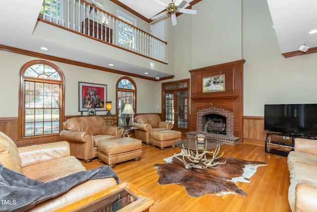 living room featuring crown molding, a towering ceiling, light hardwood / wood-style flooring, and a brick fireplace