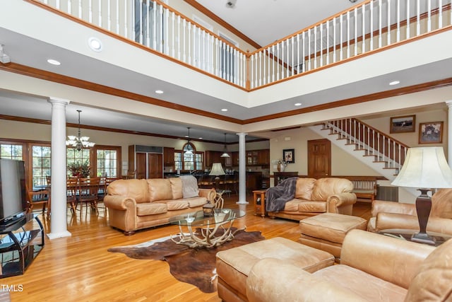 living room featuring light wood-type flooring, ornate columns, a high ceiling, ornamental molding, and a chandelier