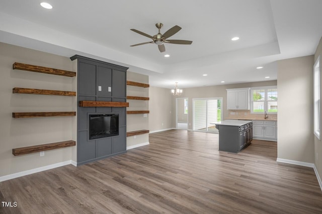 unfurnished living room with wood-type flooring, a fireplace, ceiling fan with notable chandelier, and sink