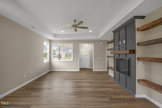 unfurnished living room with a raised ceiling, dark hardwood / wood-style flooring, ceiling fan, and a large fireplace