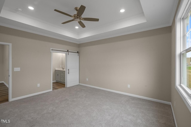 unfurnished bedroom with ensuite bathroom, a raised ceiling, a barn door, and multiple windows