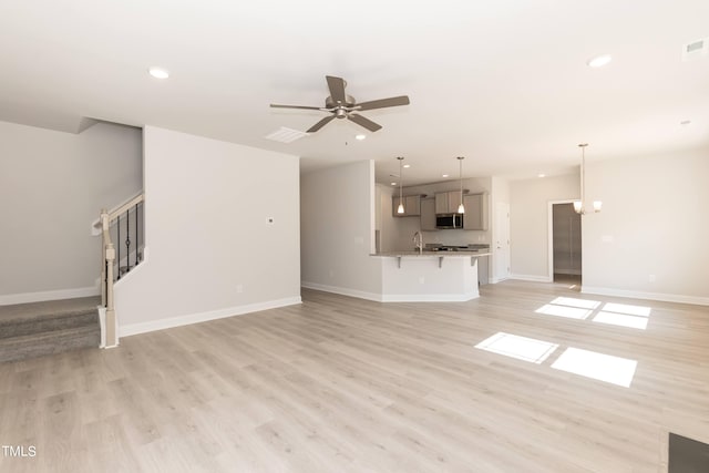 unfurnished living room with sink, ceiling fan with notable chandelier, and light hardwood / wood-style flooring