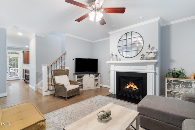 living area with wood finished floors, ornamental molding, stairway, a ceiling fan, and a fireplace with flush hearth