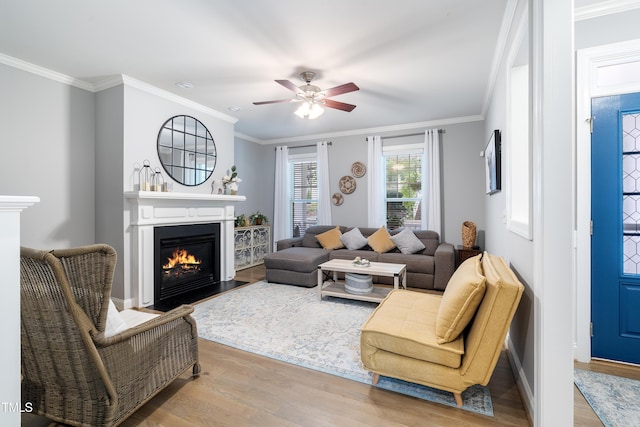 living room featuring a fireplace with flush hearth, wood finished floors, ceiling fan, ornamental molding, and baseboards