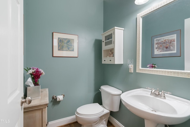 half bathroom with a sink, toilet, and baseboards