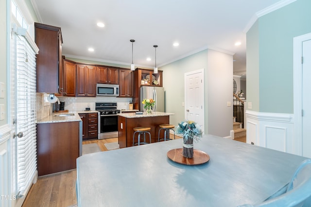 kitchen featuring appliances with stainless steel finishes, a center island, light wood-style flooring, backsplash, and decorative light fixtures