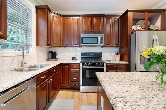 kitchen with appliances with stainless steel finishes, a sink, crown molding, light wood finished floors, and light stone countertops