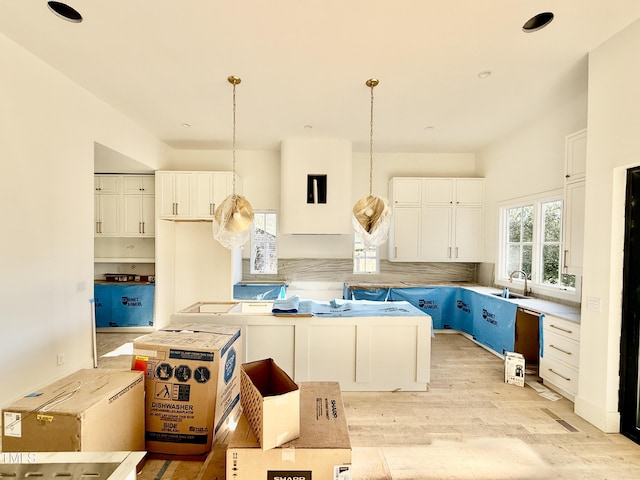 kitchen with pendant lighting, tasteful backsplash, sink, white cabinets, and light hardwood / wood-style flooring