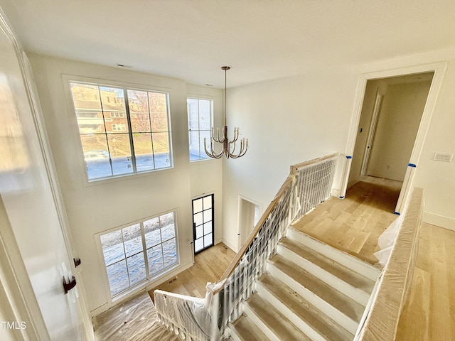 stairway with an inviting chandelier, hardwood / wood-style floors, and a high ceiling