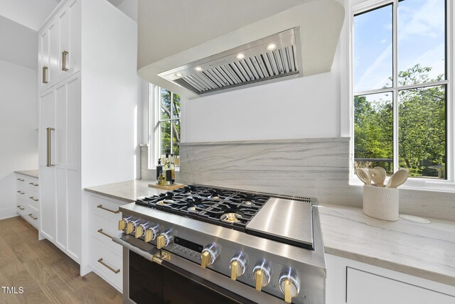 712 Daniels St, Raleigh, NC 27605 - kitchen with backsplash, wall chimney range hood, light wood-type flooring, light stone countertops, and gas stove