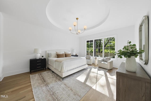 712 Daniels St, Raleigh, NC 27605 - bedroom with a tray ceiling, an inviting chandelier, light wood-style flooring, and baseboards