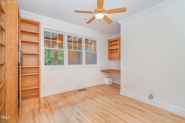 unfurnished room with built in desk, crown molding, light hardwood / wood-style flooring, and ceiling fan