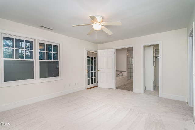 unfurnished bedroom with connected bathroom, a walk in closet, light colored carpet, and ceiling fan