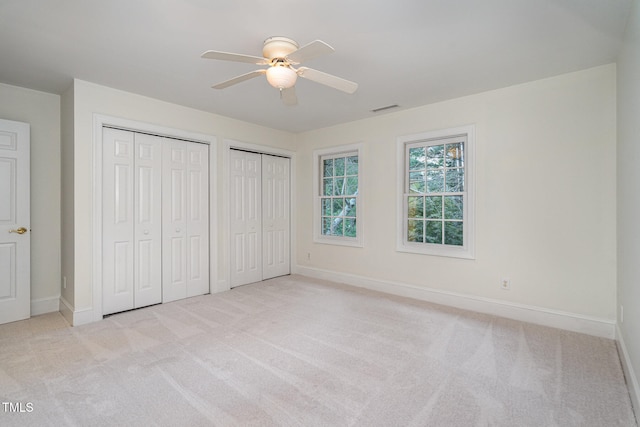 unfurnished bedroom featuring two closets, light colored carpet, and ceiling fan