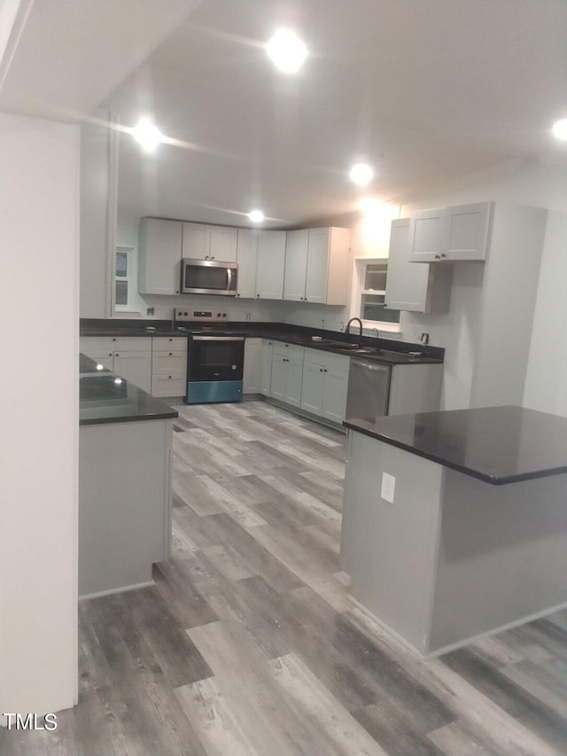 kitchen featuring wood-type flooring, sink, white cabinetry, kitchen peninsula, and appliances with stainless steel finishes