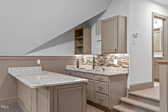 kitchen featuring sink, tasteful backsplash, wooden walls, light carpet, and light stone countertops