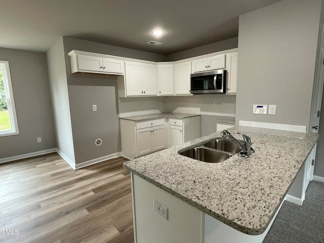 kitchen with light hardwood / wood-style floors, kitchen peninsula, sink, and white cabinets