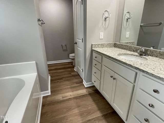 bathroom featuring a bathing tub, hardwood / wood-style flooring, vanity, and toilet