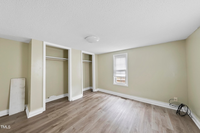 unfurnished bedroom with multiple closets, a textured ceiling, and light wood-type flooring