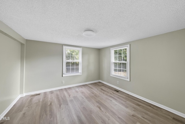 spare room featuring wood finished floors, a textured ceiling, baseboards, and visible vents