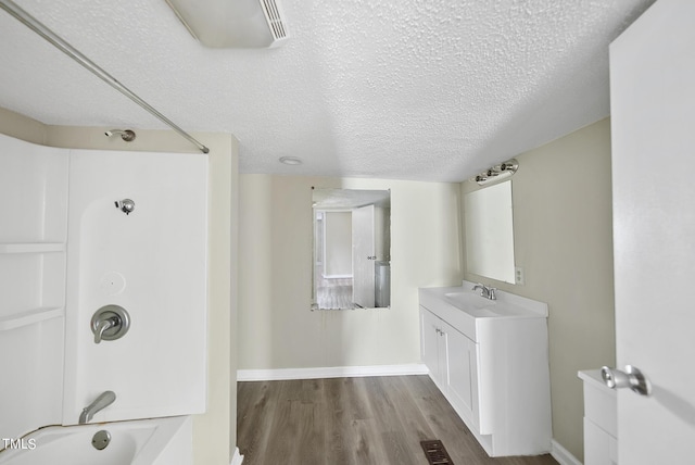 bathroom featuring wood finished floors, vanity, baseboards, shower / bathing tub combination, and a textured ceiling