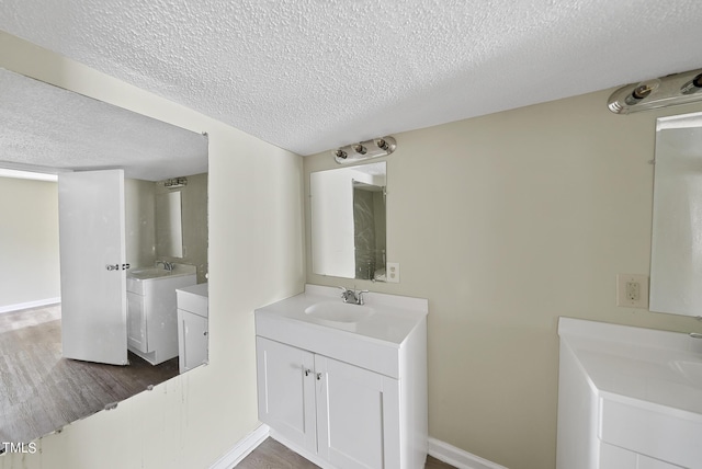 bathroom with two vanities, wood finished floors, a textured ceiling, and a sink