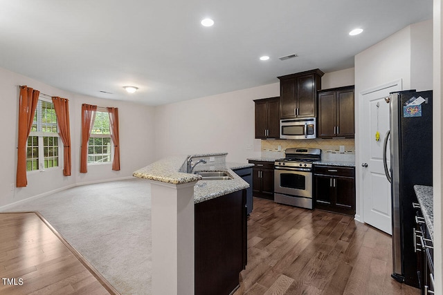 kitchen featuring sink, appliances with stainless steel finishes, dark wood-type flooring, and an island with sink