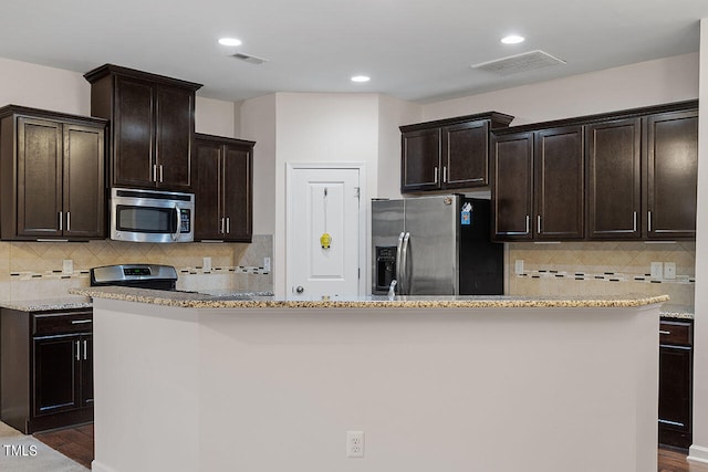 kitchen featuring tasteful backsplash, a kitchen island, stainless steel appliances, dark brown cabinetry, and dark hardwood / wood-style flooring