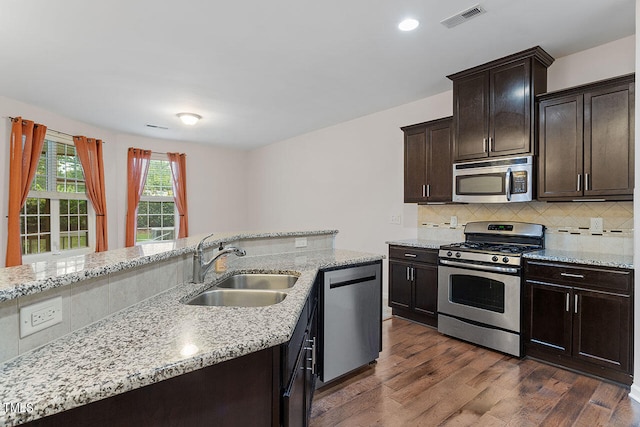 kitchen featuring appliances with stainless steel finishes, tasteful backsplash, dark hardwood / wood-style flooring, dark brown cabinets, and sink