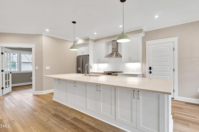 kitchen with sink, stainless steel fridge with ice dispenser, a large island with sink, wall chimney range hood, and white cabinets