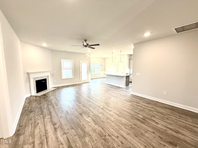 unfurnished living room featuring visible vents, a ceiling fan, wood finished floors, a high end fireplace, and baseboards