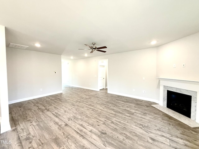 unfurnished living room featuring a high end fireplace, visible vents, baseboards, wood finished floors, and a ceiling fan