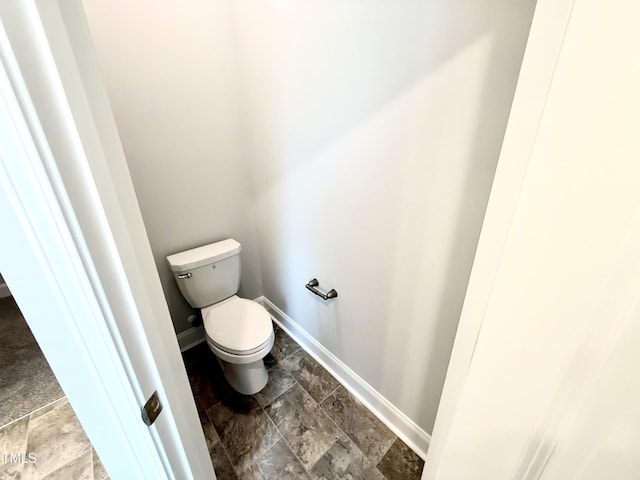 bathroom featuring stone finish flooring, baseboards, and toilet