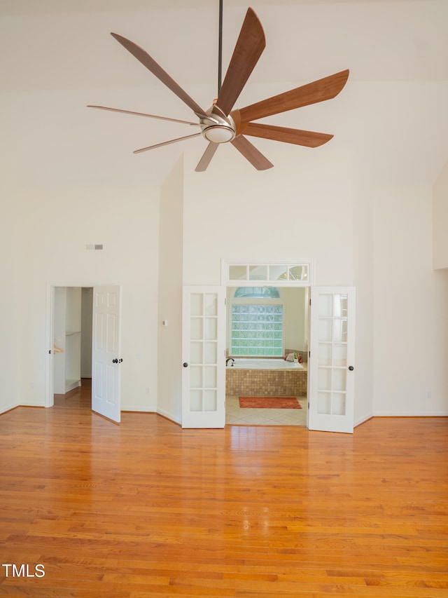 unfurnished living room with french doors, light wood-type flooring, ceiling fan, and a high ceiling